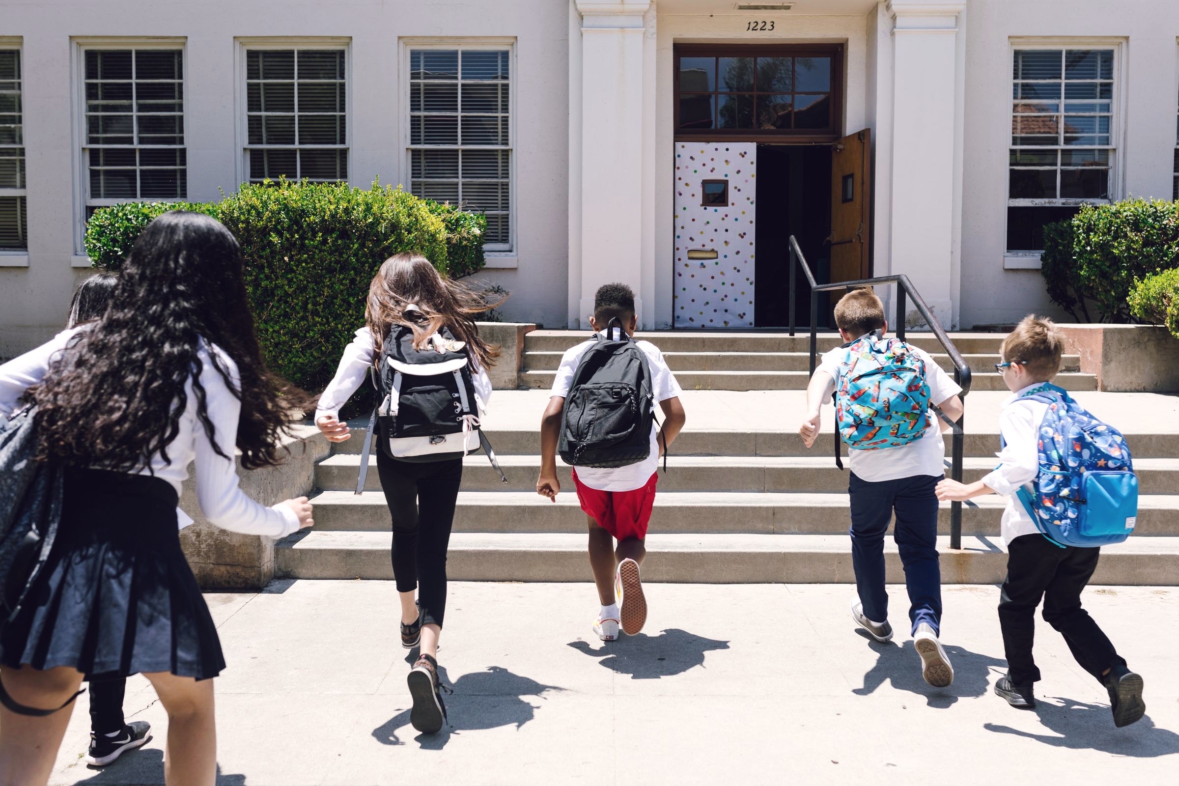 Students with backpacks running up the front steps of a school building.