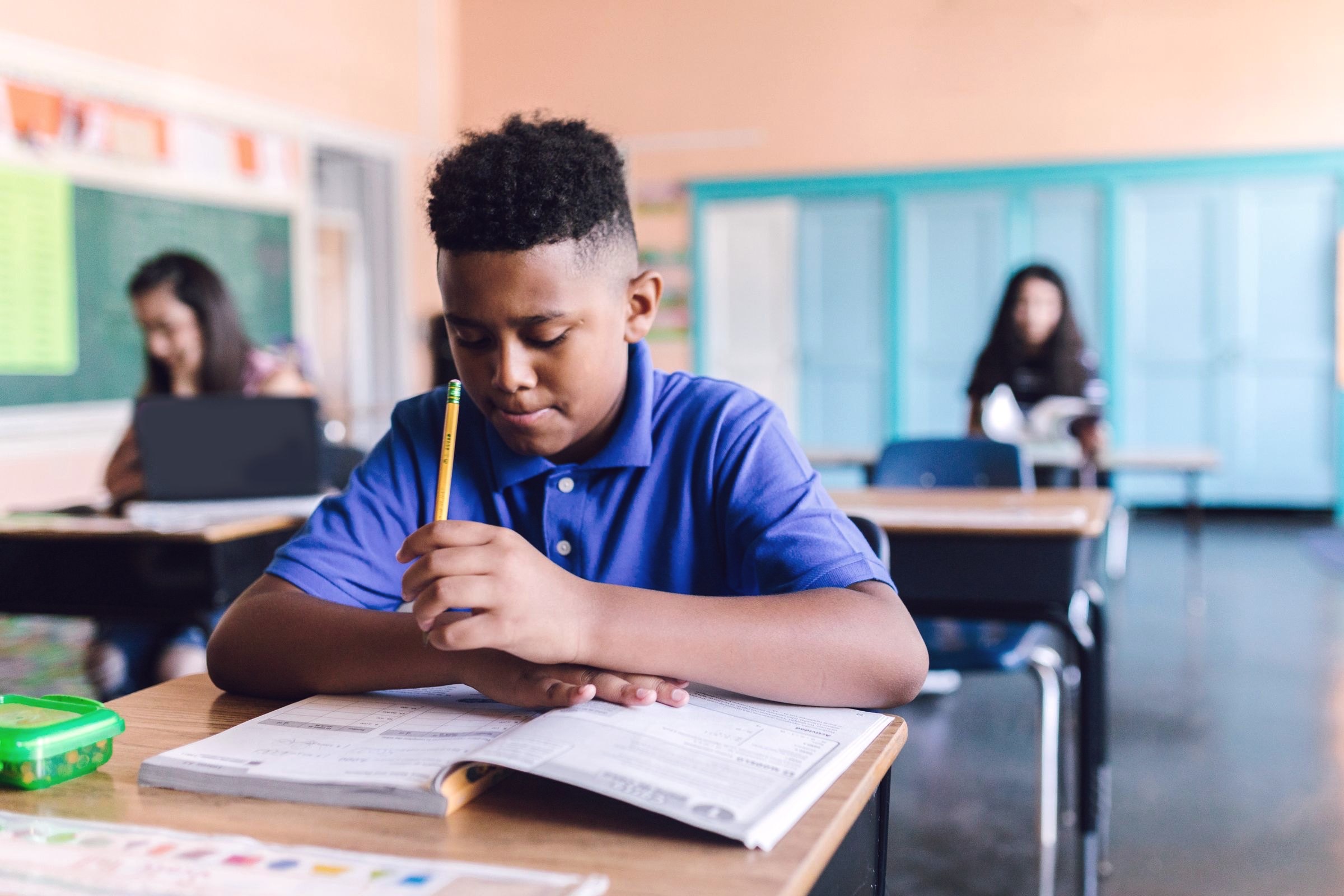A student working through a workbook at his desk in a bright classroom.